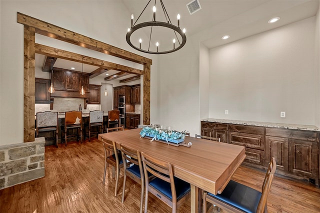 dining area featuring beam ceiling, dark hardwood / wood-style floors, and an inviting chandelier