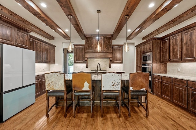 kitchen with fridge, stainless steel microwave, light hardwood / wood-style flooring, hanging light fixtures, and light stone counters