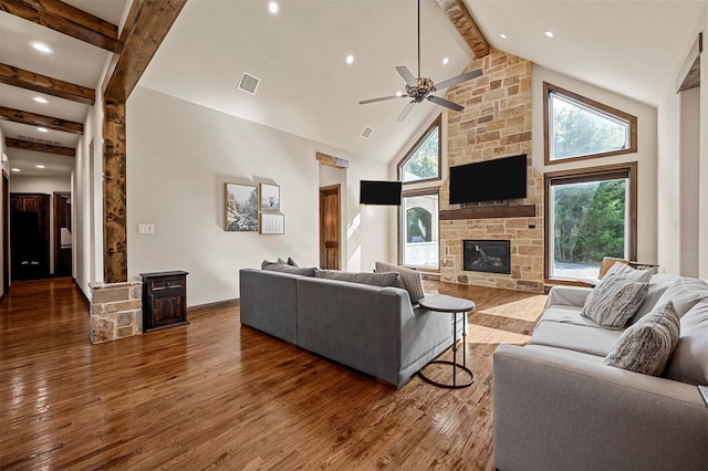 living room featuring a stone fireplace, ceiling fan, beamed ceiling, dark wood-type flooring, and high vaulted ceiling