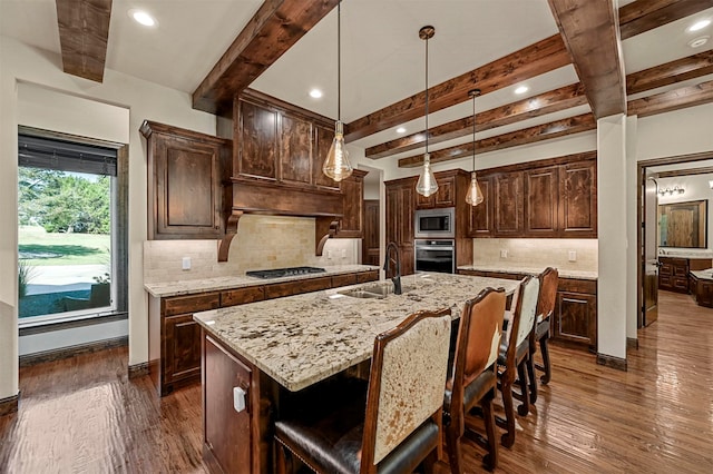 kitchen featuring a kitchen island with sink, beamed ceiling, stainless steel appliances, tasteful backsplash, and dark hardwood / wood-style flooring