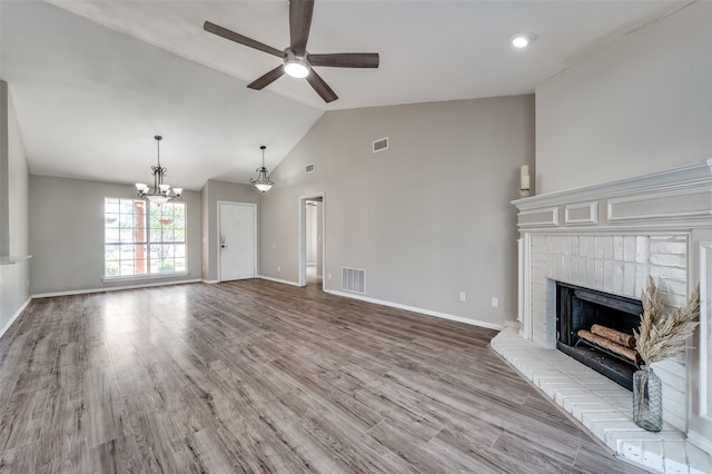 unfurnished living room with vaulted ceiling, a fireplace, light wood-type flooring, and ceiling fan with notable chandelier