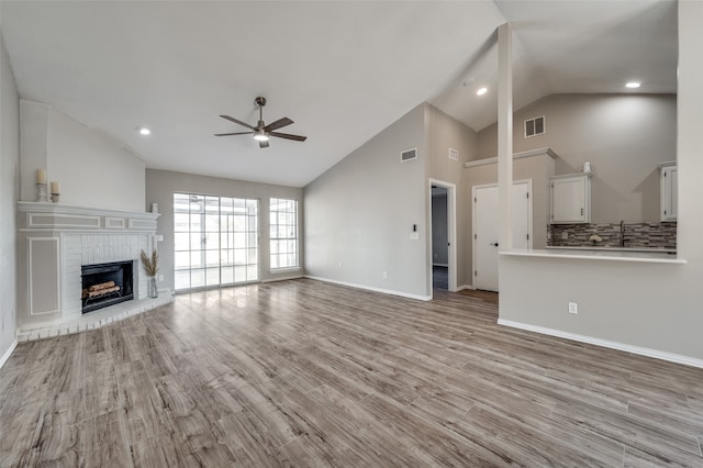 unfurnished living room with ceiling fan, high vaulted ceiling, light wood-type flooring, and a brick fireplace