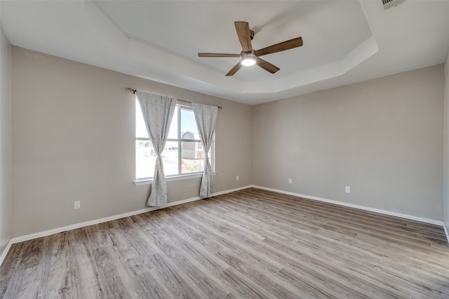 spare room with light hardwood / wood-style flooring, ceiling fan, and a raised ceiling