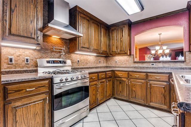 kitchen with decorative backsplash, stainless steel gas stove, a notable chandelier, and wall chimney range hood