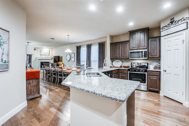 kitchen with appliances with stainless steel finishes, sink, dark brown cabinets, and light hardwood / wood-style floors