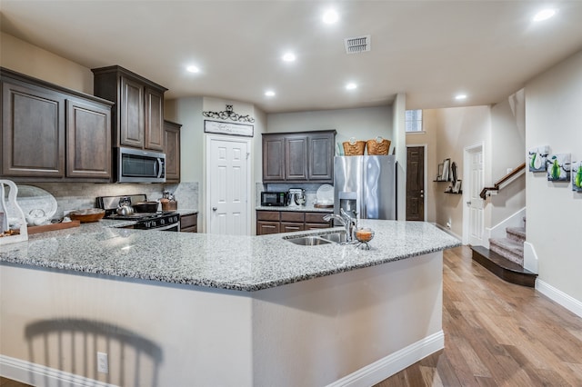 kitchen with dark brown cabinetry, stainless steel appliances, sink, and light stone counters