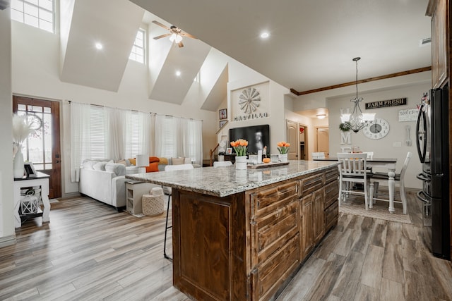 kitchen featuring hanging light fixtures, black fridge, light hardwood / wood-style flooring, ceiling fan with notable chandelier, and a center island