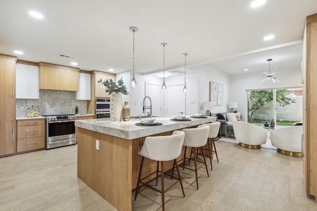 kitchen with a kitchen island with sink, light hardwood / wood-style flooring, hanging light fixtures, and stainless steel appliances