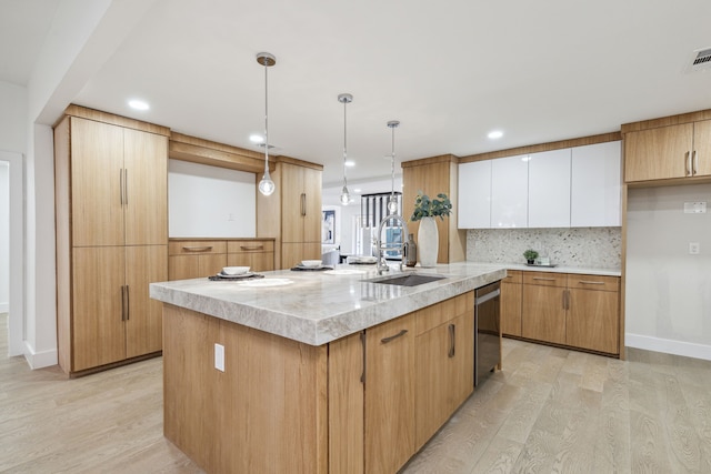 kitchen featuring light hardwood / wood-style flooring, white cabinetry, a center island with sink, and pendant lighting