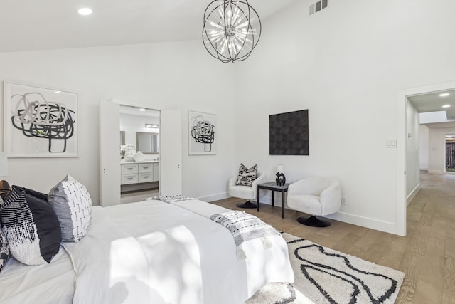 bedroom featuring a notable chandelier, ensuite bath, high vaulted ceiling, and light wood-type flooring