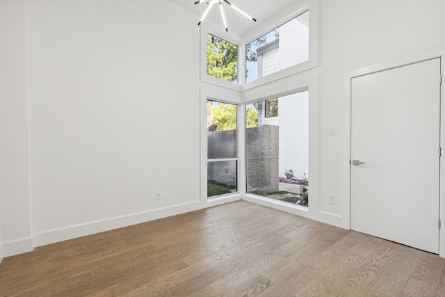 unfurnished room with light hardwood / wood-style floors, a high ceiling, and an inviting chandelier