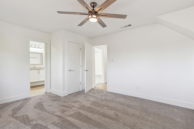 unfurnished bedroom with a closet, ceiling fan, light carpet, and ensuite bath