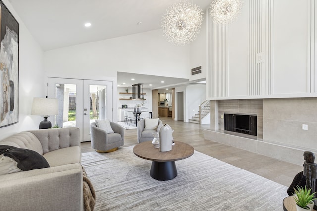 living room featuring a tiled fireplace, a notable chandelier, high vaulted ceiling, and french doors