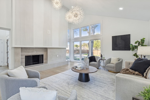 living room featuring light hardwood / wood-style flooring, a notable chandelier, a tiled fireplace, and high vaulted ceiling