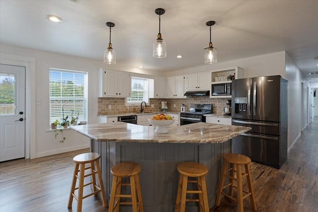 kitchen with black appliances, under cabinet range hood, a sink, white cabinets, and decorative backsplash