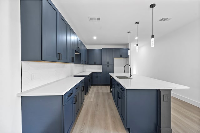 kitchen with sink, light wood-type flooring, pendant lighting, decorative backsplash, and a center island with sink