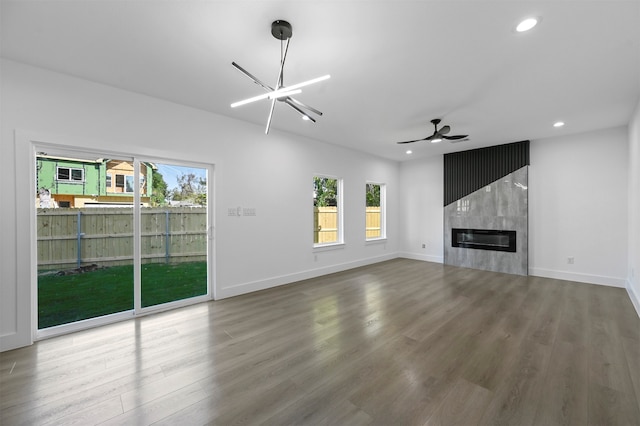 unfurnished living room with ceiling fan with notable chandelier, wood-type flooring, and a large fireplace