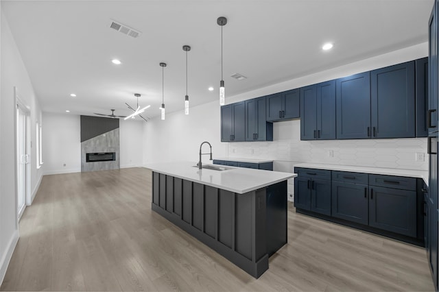 kitchen with sink, light wood-type flooring, backsplash, hanging light fixtures, and a center island with sink