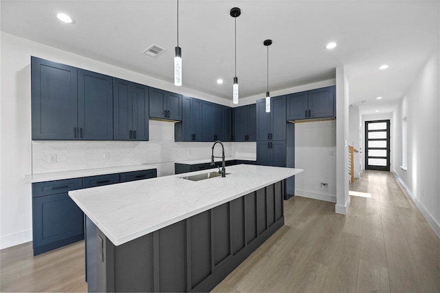 kitchen with light hardwood / wood-style floors, light stone countertops, sink, and a center island with sink