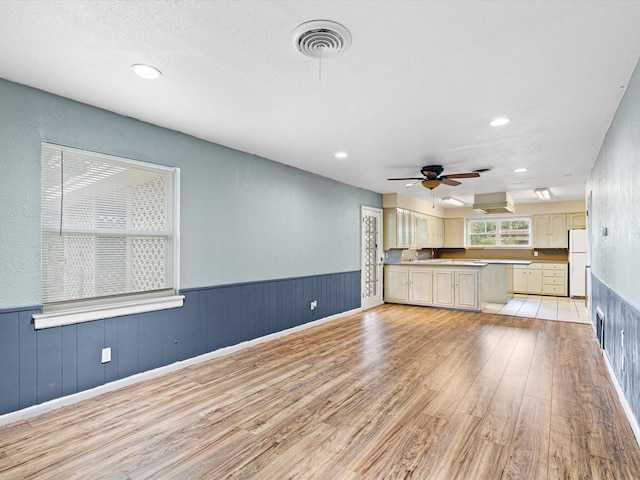 unfurnished living room with ceiling fan, a textured ceiling, and light wood-type flooring