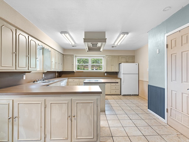 kitchen with light tile patterned flooring, sink, kitchen peninsula, white fridge, and cream cabinetry