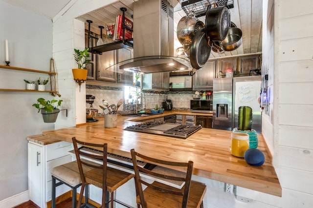 kitchen with sink, appliances with stainless steel finishes, tasteful backsplash, butcher block countertops, and island exhaust hood