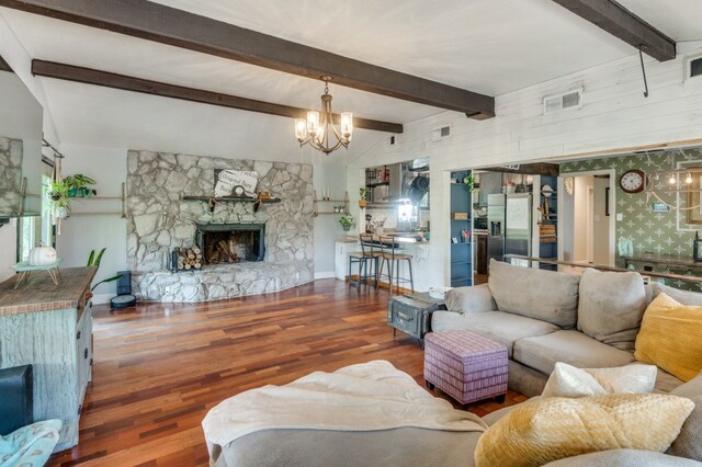 living room with vaulted ceiling with beams, dark hardwood / wood-style floors, a stone fireplace, and a chandelier