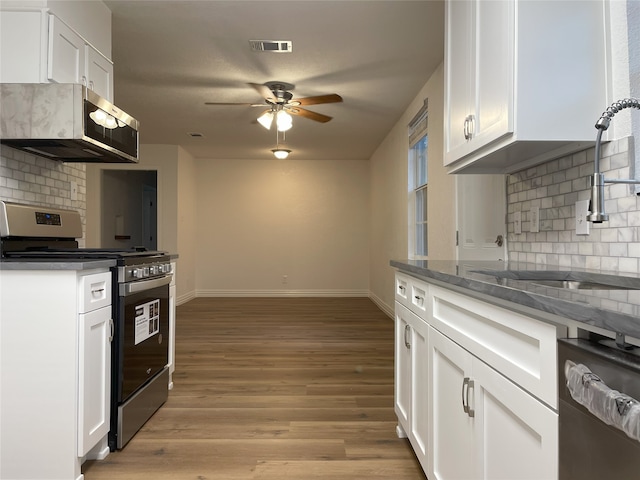 kitchen with light wood-type flooring, tasteful backsplash, exhaust hood, white cabinets, and stainless steel range with gas cooktop