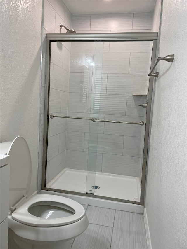 bathroom featuring tile patterned flooring, toilet, and a shower with door