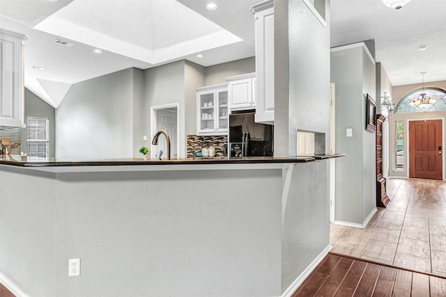 kitchen with kitchen peninsula, black refrigerator with ice dispenser, sink, white cabinetry, and light hardwood / wood-style floors