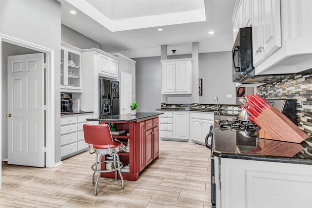 kitchen featuring black appliances, a textured ceiling, a center island, white cabinets, and a breakfast bar