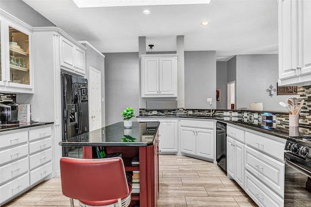 kitchen with sink, black appliances, a kitchen bar, a center island, and white cabinets