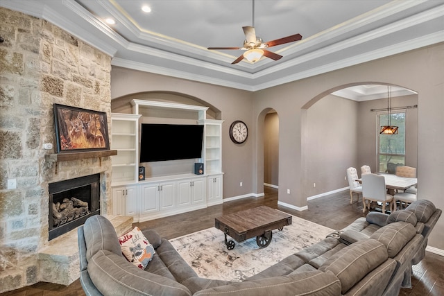 living room with a raised ceiling, ceiling fan, ornamental molding, dark wood-type flooring, and a fireplace