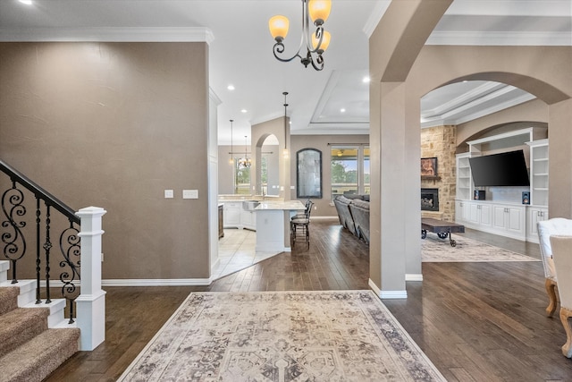 entryway featuring dark wood-type flooring, a stone fireplace, crown molding, and an inviting chandelier