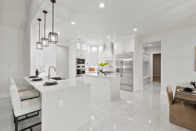 kitchen featuring built in appliances, premium range hood, a kitchen island, a sink, and white cabinets