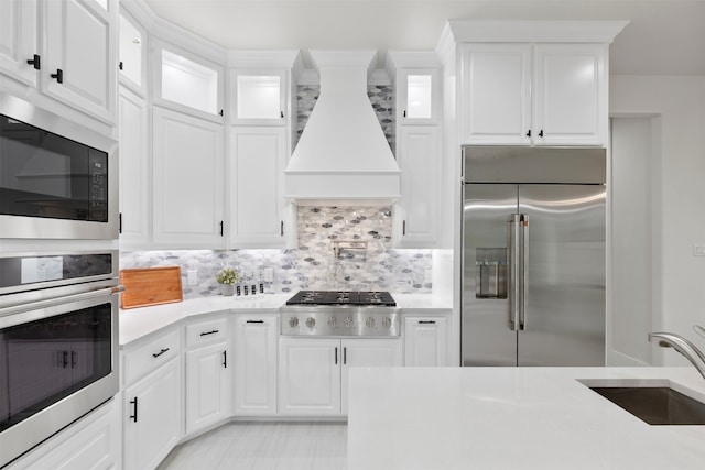 kitchen with light countertops, a sink, custom exhaust hood, and built in appliances