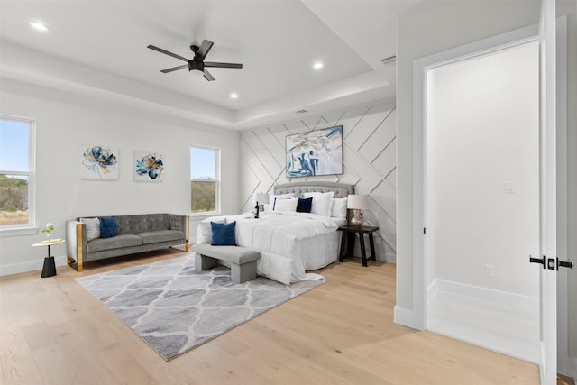 bedroom featuring recessed lighting, a raised ceiling, multiple windows, and light wood-style flooring