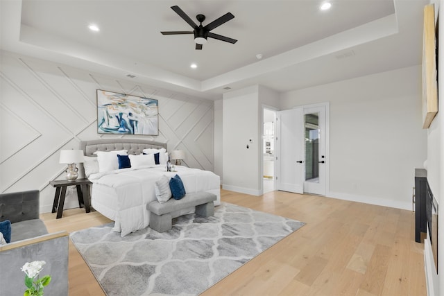 bedroom with a tray ceiling, recessed lighting, light wood-style flooring, and baseboards