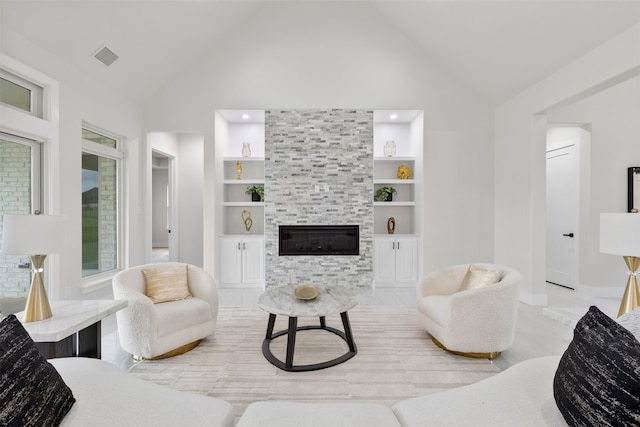 living area with high vaulted ceiling, built in shelves, a tiled fireplace, and visible vents