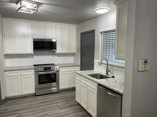 kitchen with decorative backsplash, white cabinets, dark hardwood / wood-style flooring, appliances with stainless steel finishes, and sink