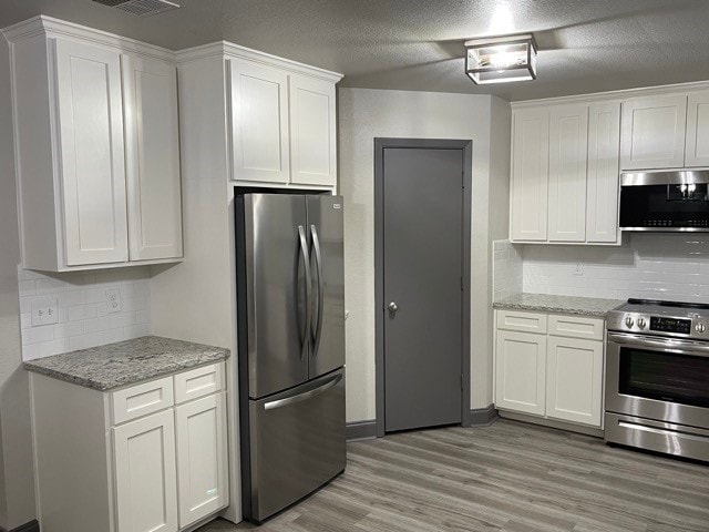 kitchen featuring decorative backsplash, appliances with stainless steel finishes, white cabinets, and light hardwood / wood-style floors