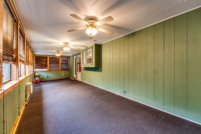 carpeted empty room featuring wooden walls and ceiling fan