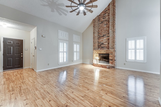 unfurnished living room with ceiling fan, a textured ceiling, high vaulted ceiling, light wood-type flooring, and a fireplace