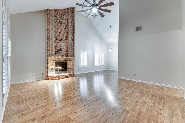 unfurnished living room featuring ceiling fan, a textured ceiling, high vaulted ceiling, light wood-type flooring, and a fireplace