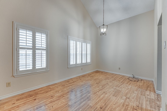 spare room with light hardwood / wood-style floors, an inviting chandelier, high vaulted ceiling, and a wealth of natural light