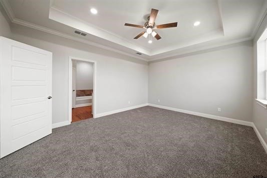 unfurnished bedroom featuring ceiling fan, a raised ceiling, connected bathroom, dark carpet, and crown molding