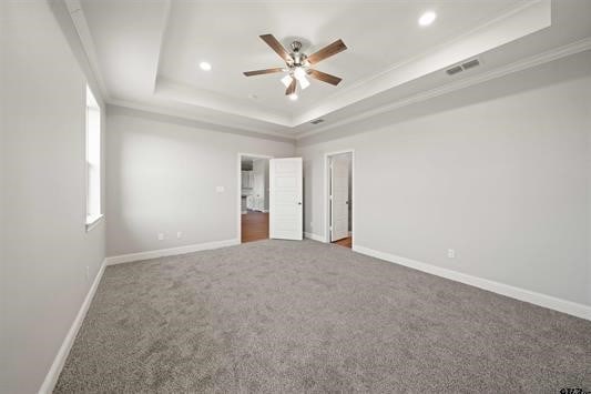 unfurnished bedroom featuring ceiling fan, a raised ceiling, ornamental molding, and carpet floors