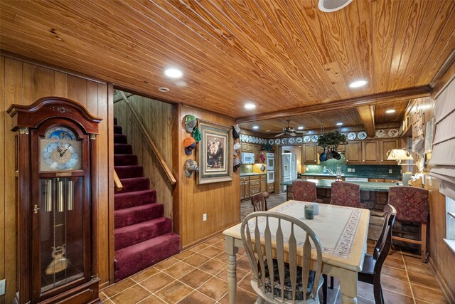 tiled dining space featuring wood ceiling, beamed ceiling, wooden walls, sink, and ceiling fan