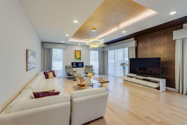 living room with a healthy amount of sunlight, light hardwood / wood-style floors, and a tray ceiling