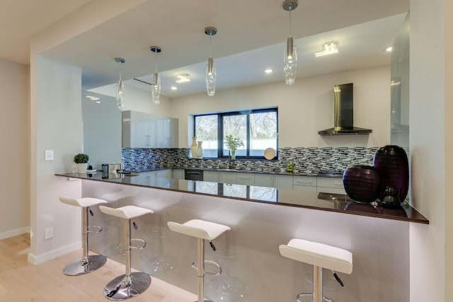 kitchen featuring wall chimney range hood, a kitchen breakfast bar, kitchen peninsula, light hardwood / wood-style floors, and decorative backsplash